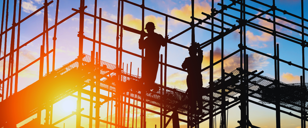 Two construction workers on scaffolding with the sunrise in the background