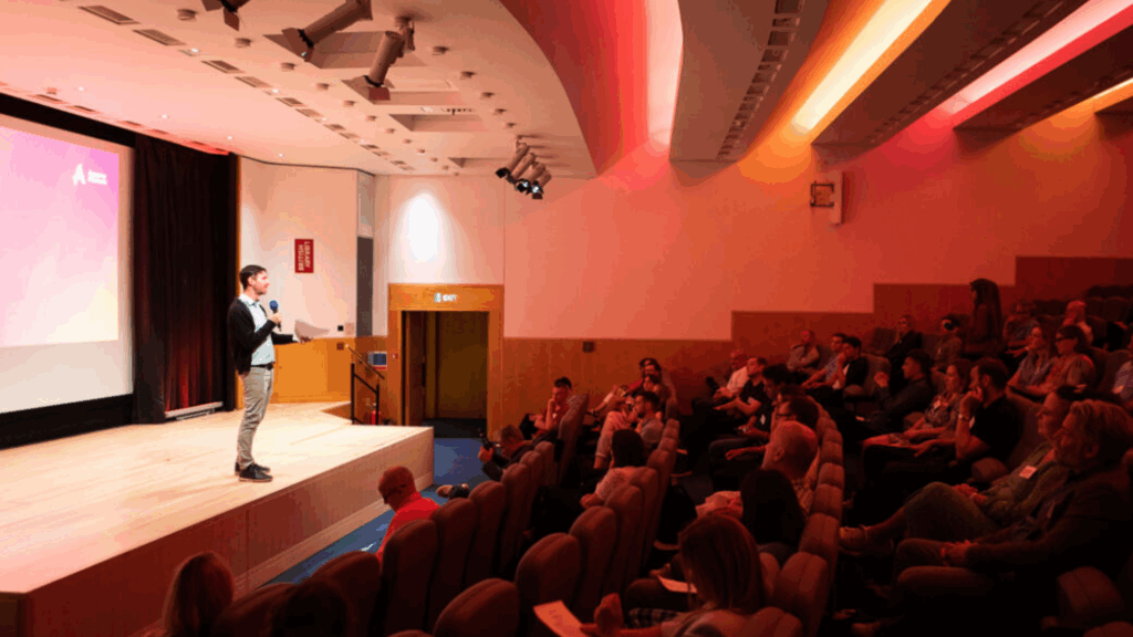 Speaker presenting at a client services conference, sharing strategies for keeping clients happy with attentive audience engagement.