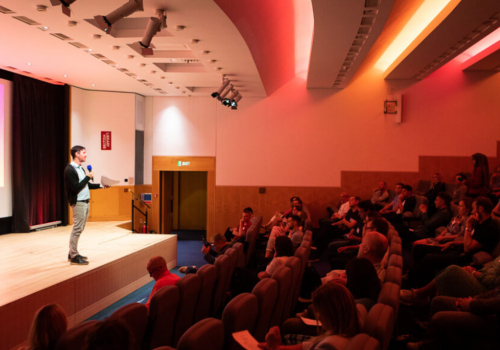Speaker presenting at a client services conference, sharing strategies for keeping clients happy with attentive audience engagement.