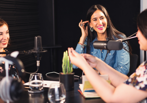 A group of three women in a podcast environment with microphones.